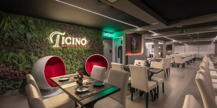 Salão interno do Ticino com parede verde viva, cadeiras-ovo vermelhas e neon